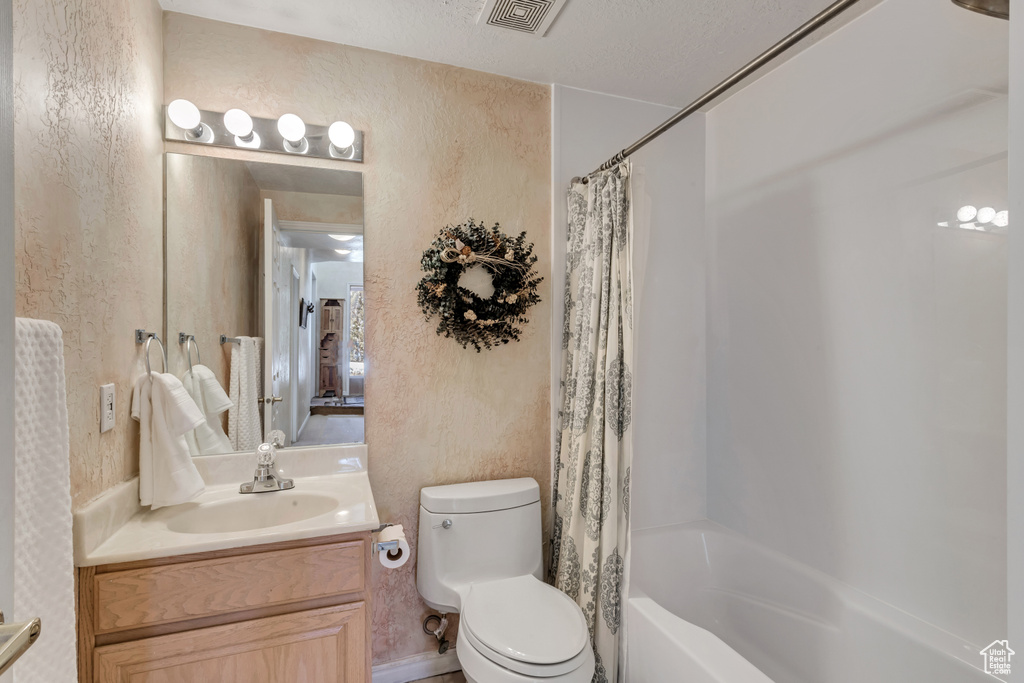 Full bathroom featuring large vanity, toilet, a textured ceiling, and shower / bath combination with curtain