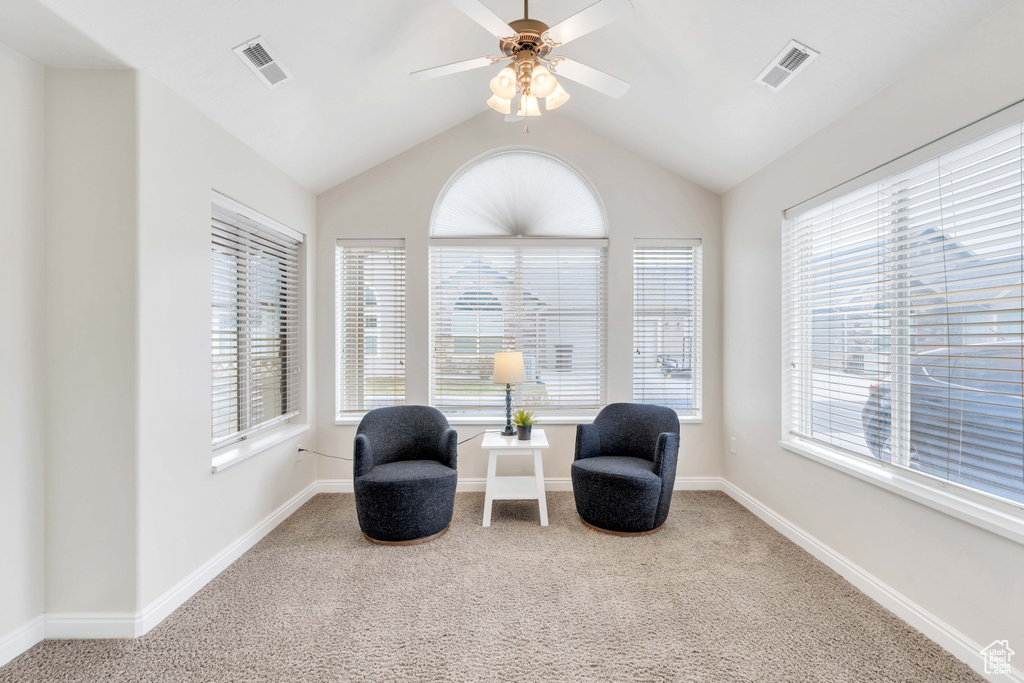 Living area featuring plenty of natural light, lofted ceiling, ceiling fan, and light colored carpet