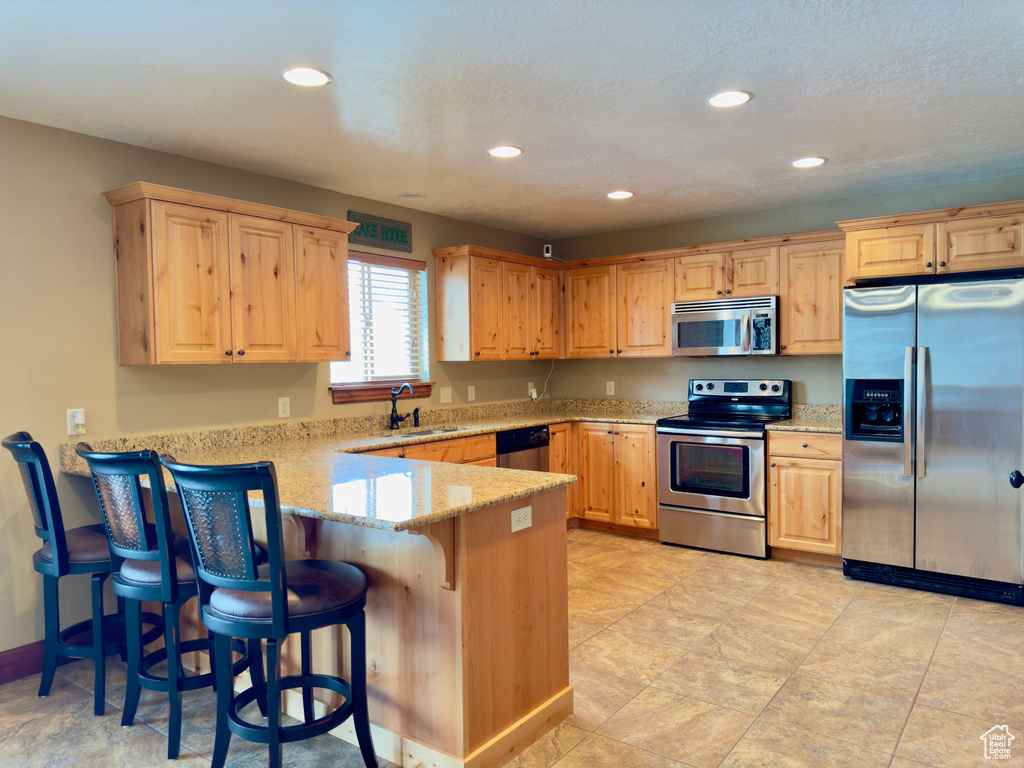Kitchen featuring kitchen peninsula, sink, light tile floors, a kitchen breakfast bar, and stainless steel appliances