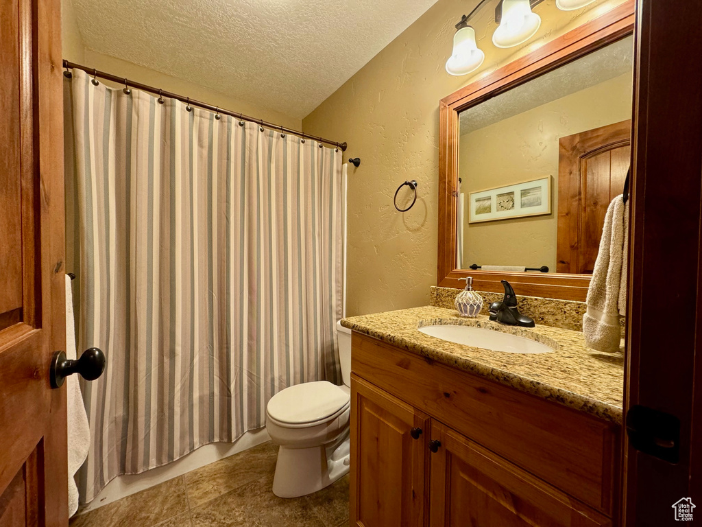 Full bathroom featuring toilet, shower / tub combo with curtain, tile flooring, a textured ceiling, and vanity