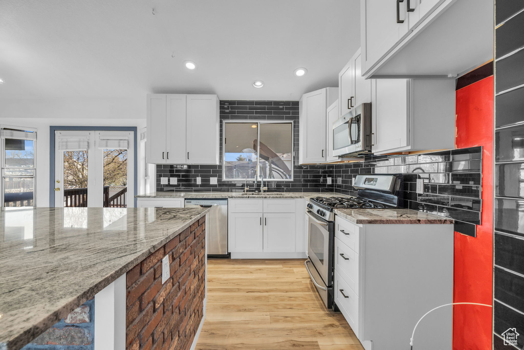 Kitchen featuring tasteful backsplash, stainless steel appliances, white cabinetry, and light hardwood / wood-style flooring