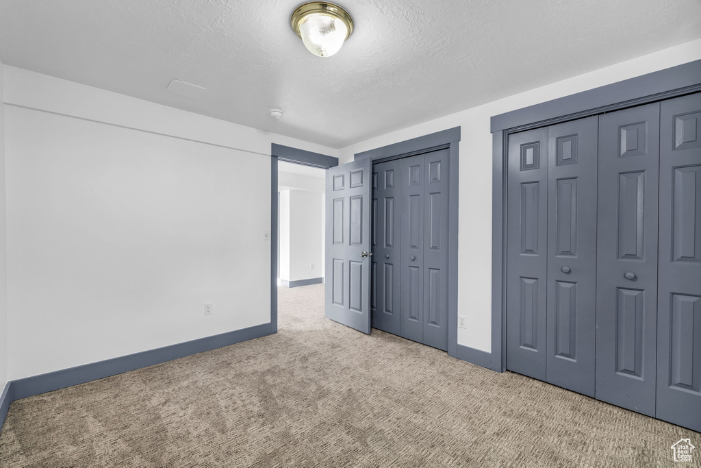 Unfurnished bedroom with light carpet, a textured ceiling, and multiple closets