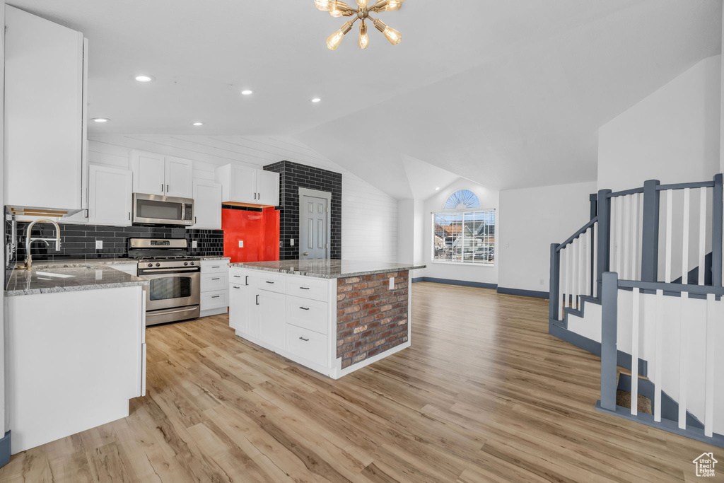 Kitchen featuring white cabinetry, appliances with stainless steel finishes, light hardwood / wood-style floors, a chandelier, and light stone counters