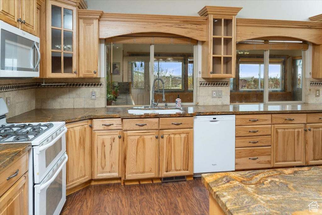 Kitchen with dark hardwood / wood-style floors, white appliances, sink, dark stone counters, and tasteful backsplash