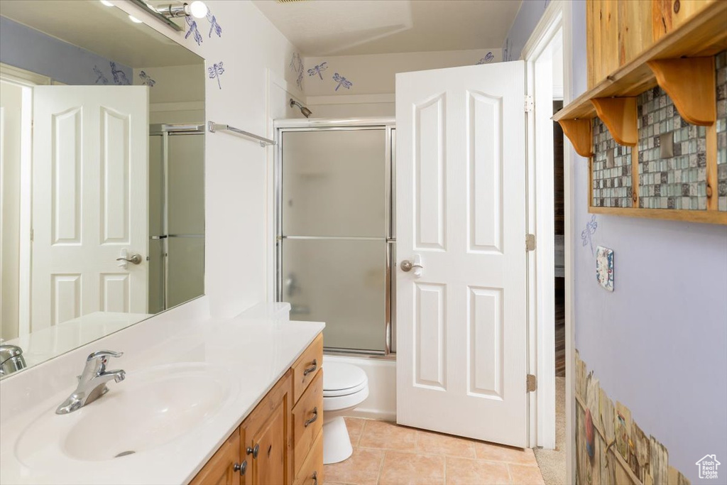 Full bathroom with toilet, shower / bath combination with glass door, tile floors, and vanity