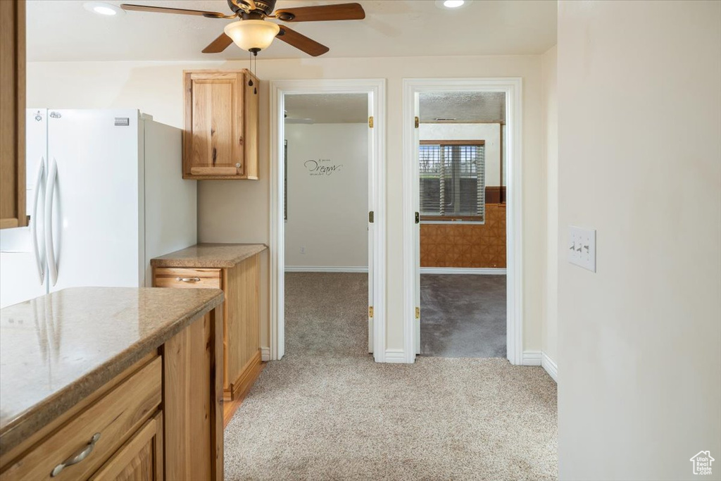 Kitchen with light colored carpet, ceiling fan, white refrigerator, and light stone counters