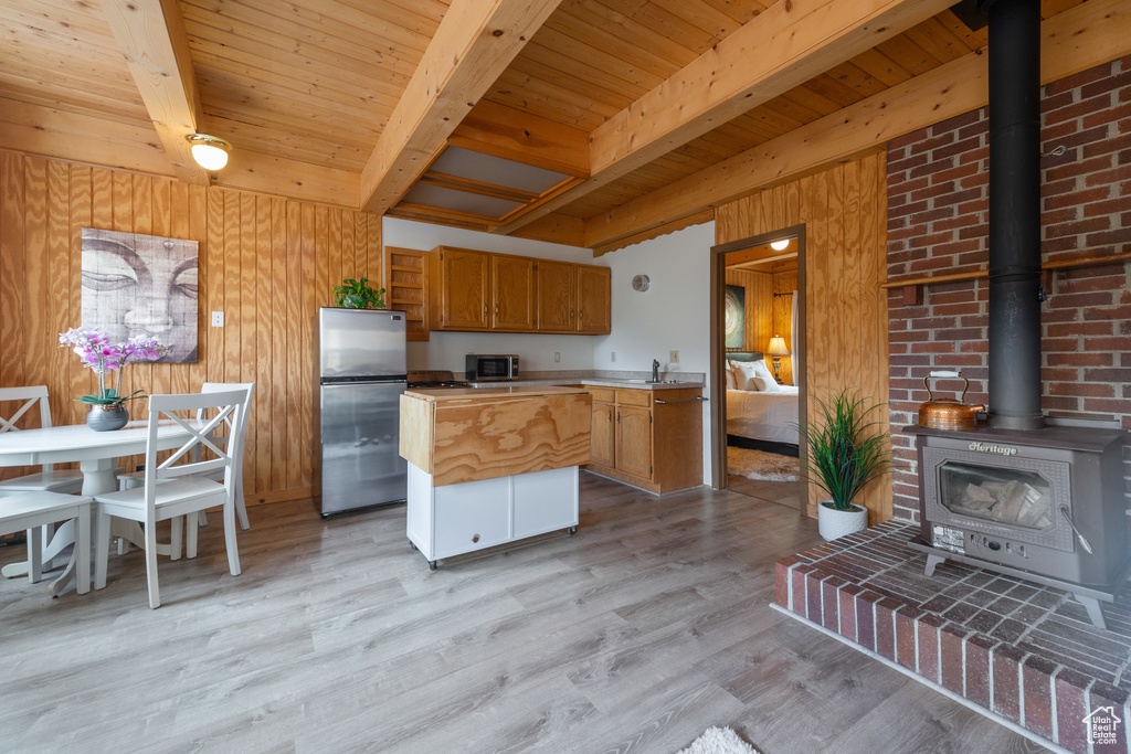 Kitchen featuring beam ceiling, light hardwood / wood-style floors, stainless steel appliances, and a wood stove