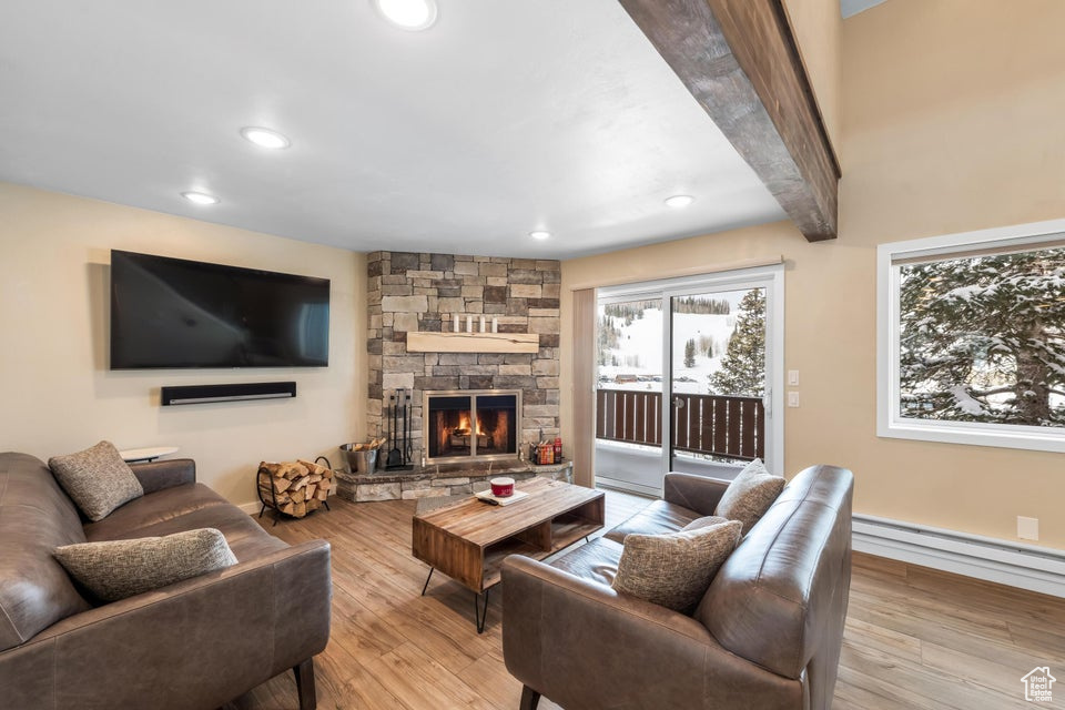 Living room featuring beam ceiling, light hardwood / wood-style floors, a baseboard heating unit, and a fireplace