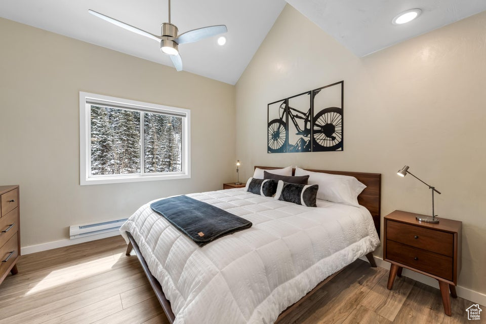 Bedroom featuring high vaulted ceiling, light hardwood / wood-style flooring, ceiling fan, and baseboard heating