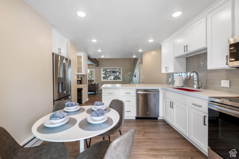 Kitchen featuring kitchen peninsula, backsplash, sink, stainless steel appliances, and hardwood / wood-style flooring