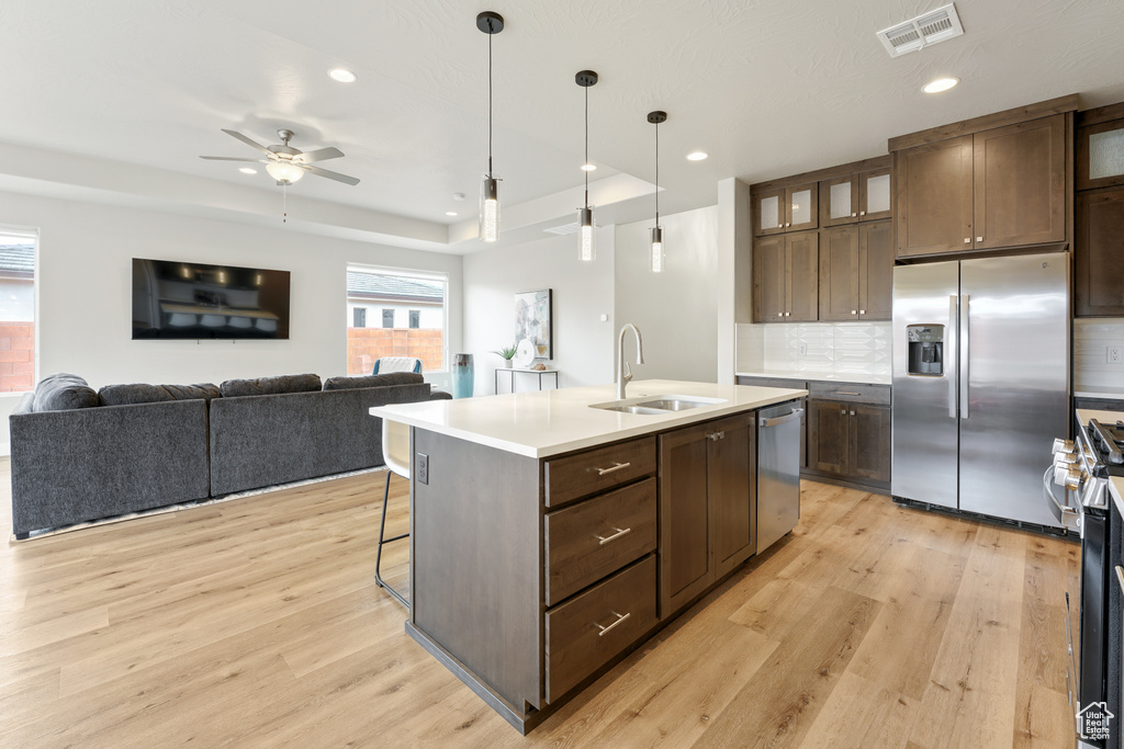 Kitchen featuring ceiling fan, a raised ceiling, a center island with sink, and light hardwood / wood-style flooring