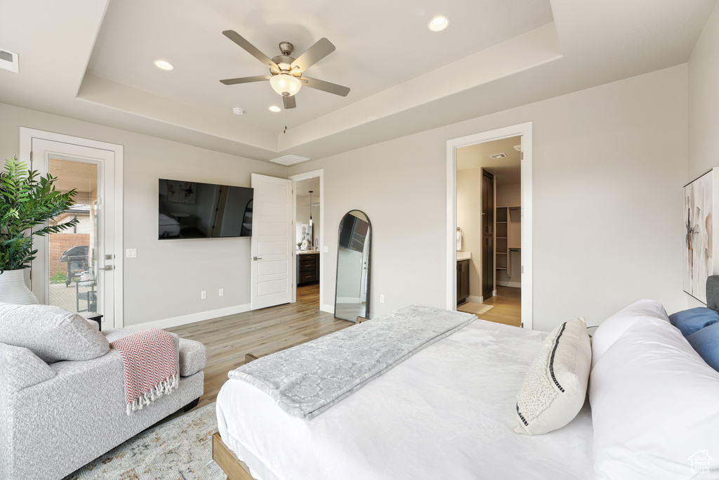 Bedroom with a tray ceiling, ceiling fan, light wood-type flooring, and ensuite bathroom