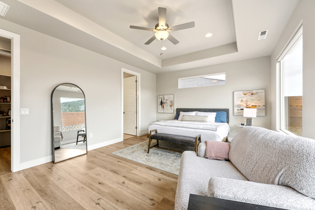 Bedroom featuring a raised ceiling, light hardwood / wood-style floors, and ceiling fan