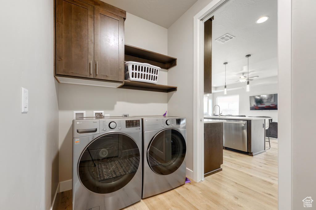 Laundry area with ceiling fan, hookup for a washing machine, cabinets, washer and dryer, and light wood-type flooring