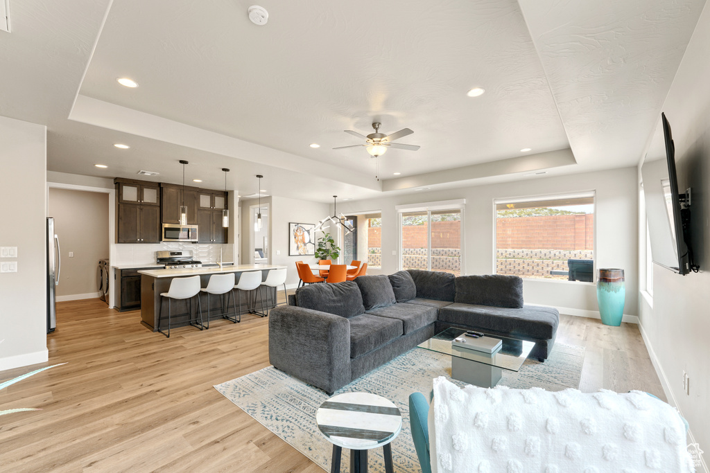 Living room featuring ceiling fan, a tray ceiling, and light hardwood / wood-style flooring