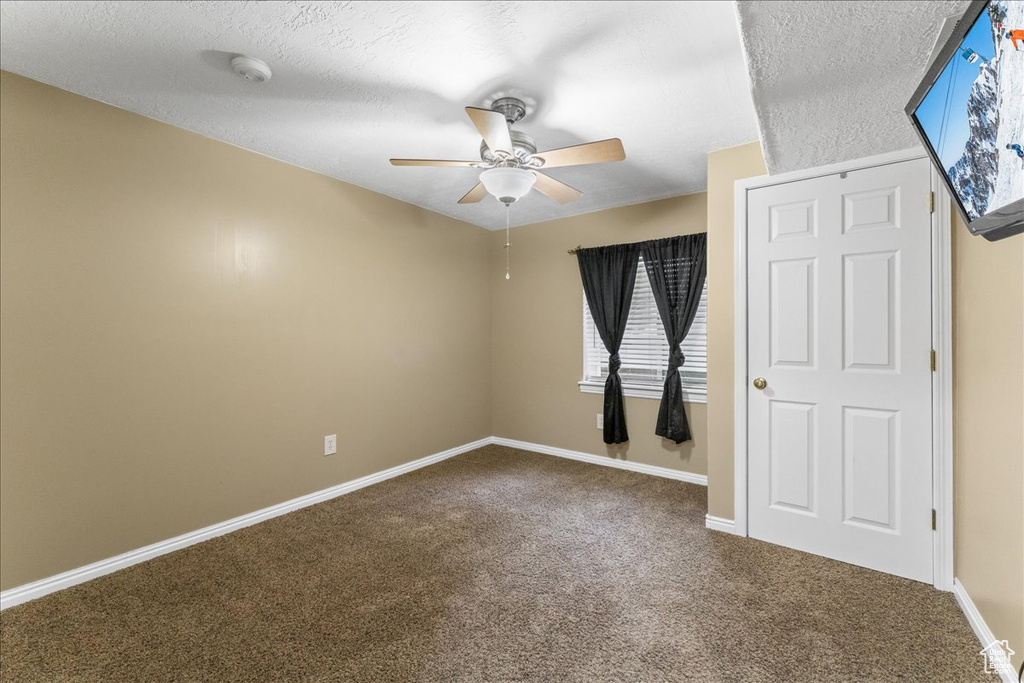 Unfurnished bedroom with dark colored carpet, ceiling fan, and a textured ceiling