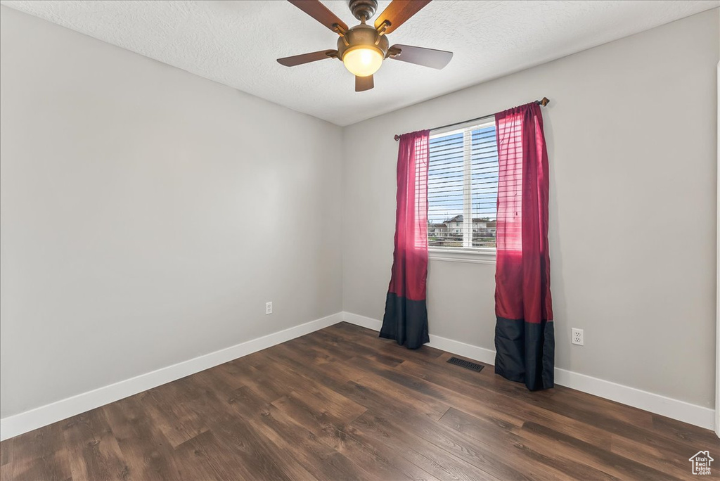 Empty room with ceiling fan, a textured ceiling, and dark hardwood / wood-style flooring