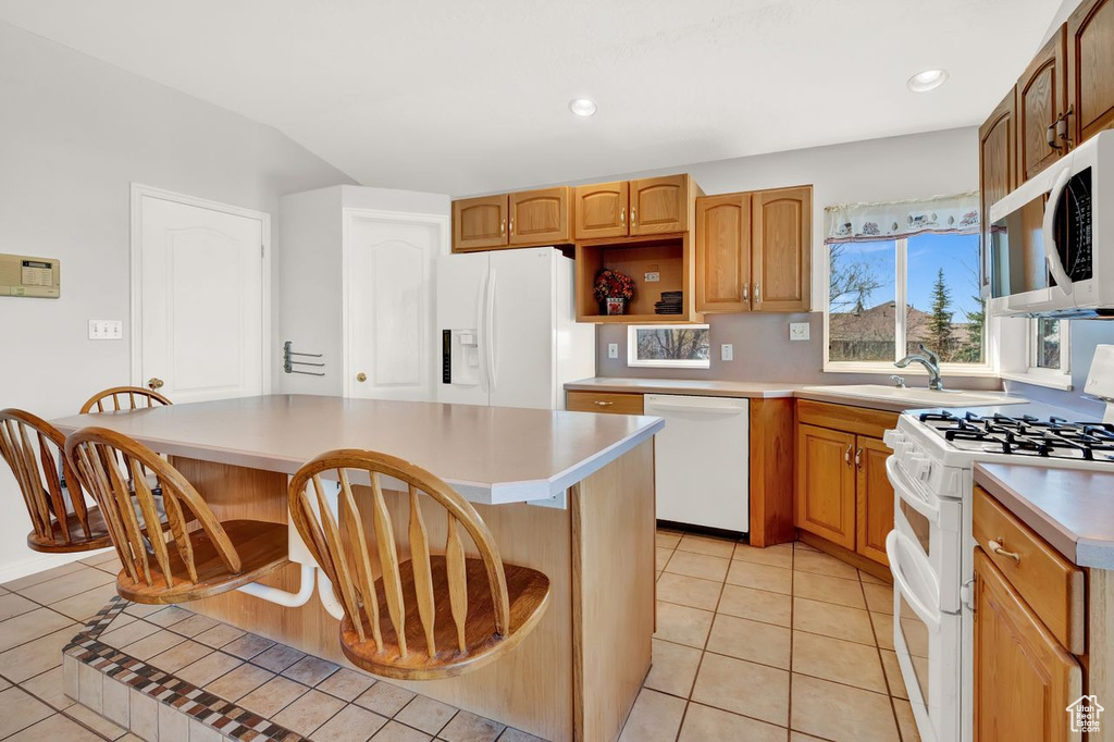 Kitchen with a kitchen bar, a kitchen island, white appliances, and light tile floors