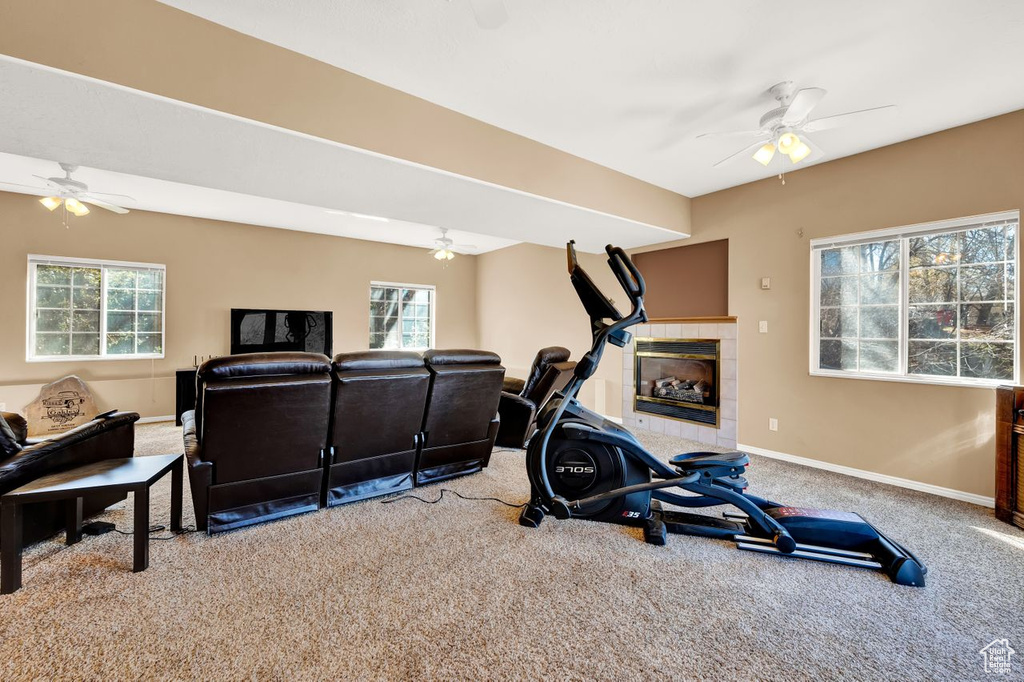 Exercise area featuring a tiled fireplace, light carpet, and ceiling fan