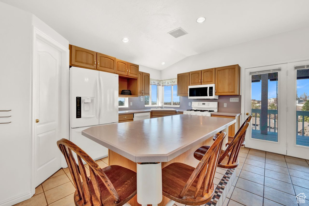Kitchen featuring white appliances, light tile floors, a kitchen breakfast bar, lofted ceiling, and a center island
