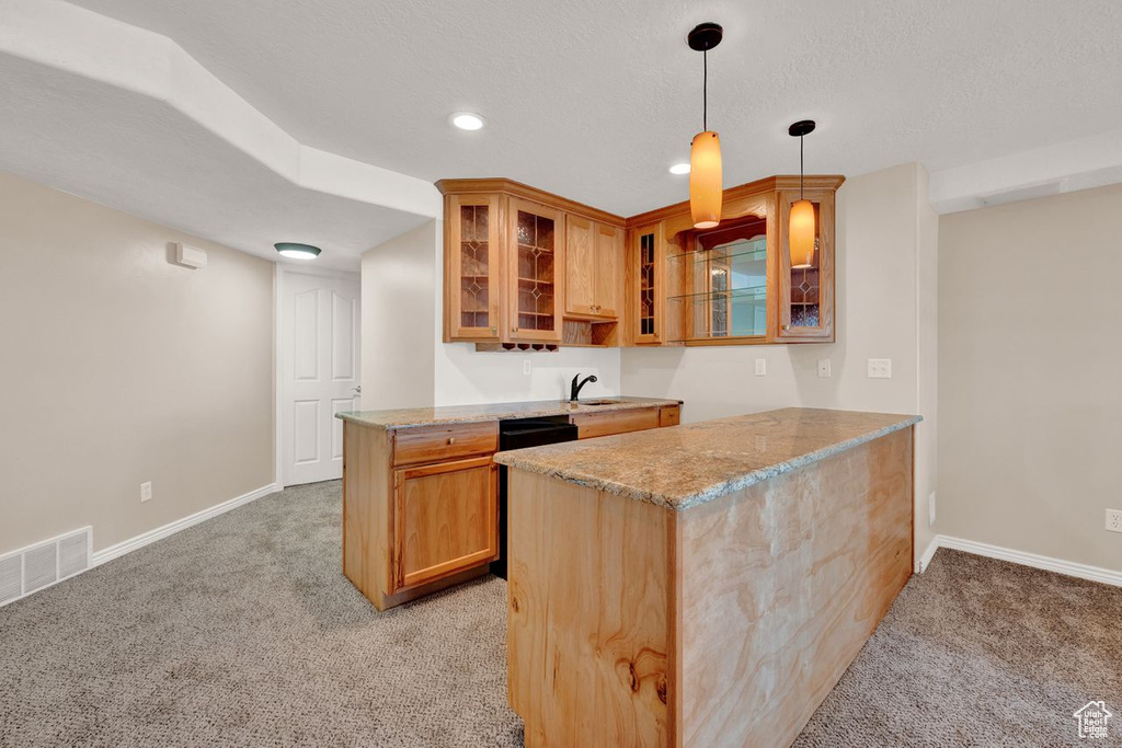 Kitchen with kitchen peninsula, sink, light stone countertops, light carpet, and decorative light fixtures