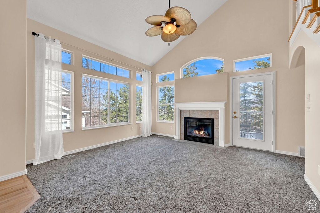 Unfurnished living room with dark carpet, ceiling fan, high vaulted ceiling, and a fireplace