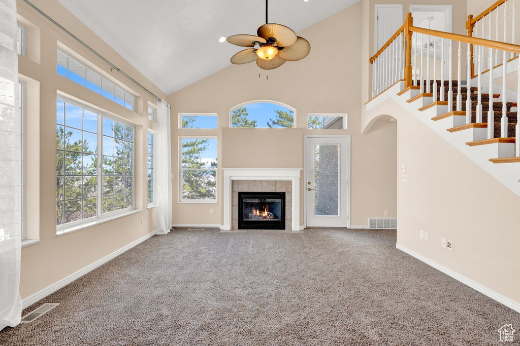 Unfurnished living room featuring a tiled fireplace, plenty of natural light, and dark colored carpet