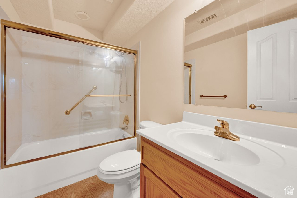 Full bathroom featuring vanity, hardwood / wood-style floors, a textured ceiling, bath / shower combo with glass door, and toilet
