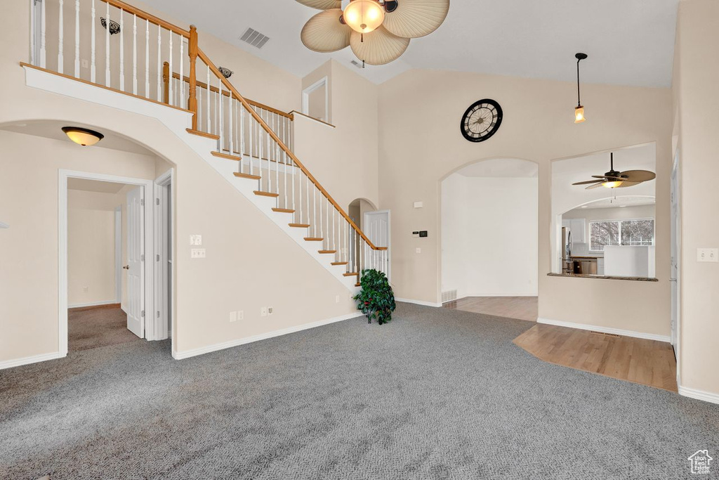 Carpeted foyer entrance with high vaulted ceiling and ceiling fan