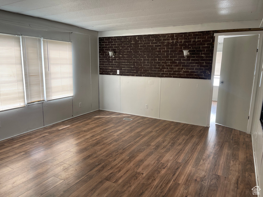 Unfurnished room featuring brick wall and dark wood-type flooring