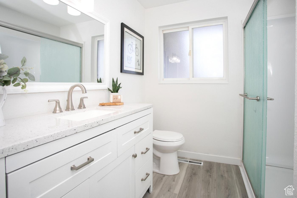 Bathroom with oversized vanity, toilet, a shower with door, and hardwood / wood-style flooring
