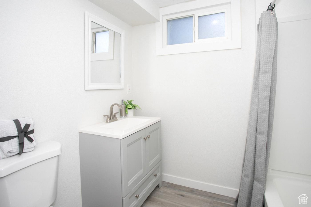 Full bathroom featuring shower / bath combination with curtain, toilet, vanity, and hardwood / wood-style flooring