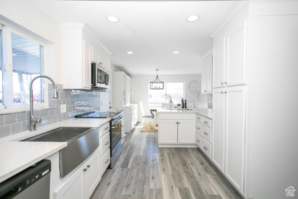 Kitchen featuring pendant lighting, white cabinets, appliances with stainless steel finishes, light hardwood / wood-style floors, and tasteful backsplash