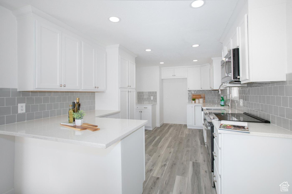 Kitchen featuring kitchen peninsula, white cabinetry, backsplash, light wood-type flooring, and sink