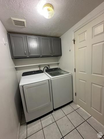 Washroom featuring cabinets, a textured ceiling, separate washer and dryer, and light tile floors