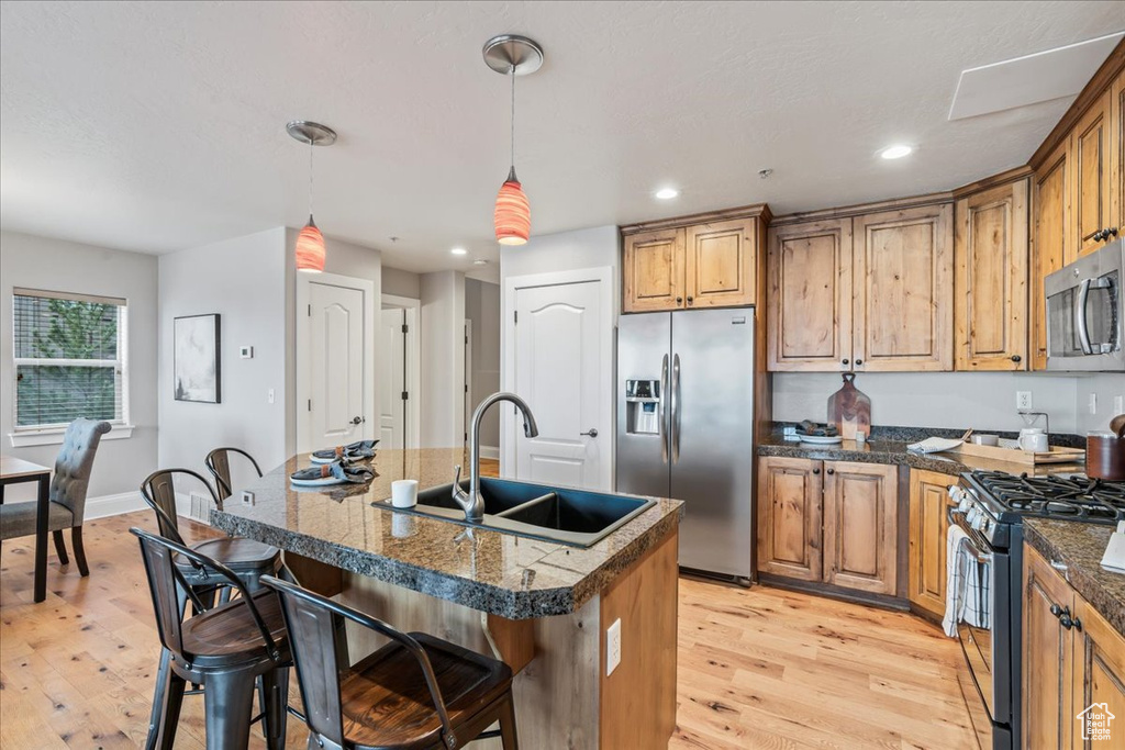 Kitchen with a kitchen bar, light hardwood / wood-style flooring, appliances with stainless steel finishes, hanging light fixtures, and a kitchen island with sink