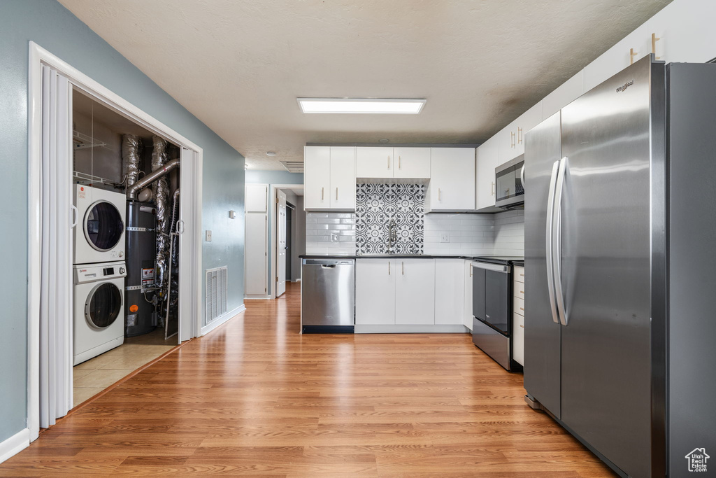 Kitchen featuring light wood-type flooring, stacked washing maching and dryer, stainless steel appliances, and white cabinetry