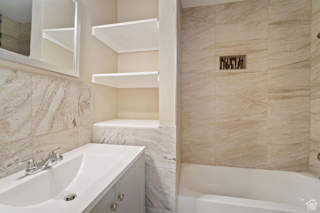 Bathroom featuring tiled shower / bath, vanity with extensive cabinet space, and tile walls