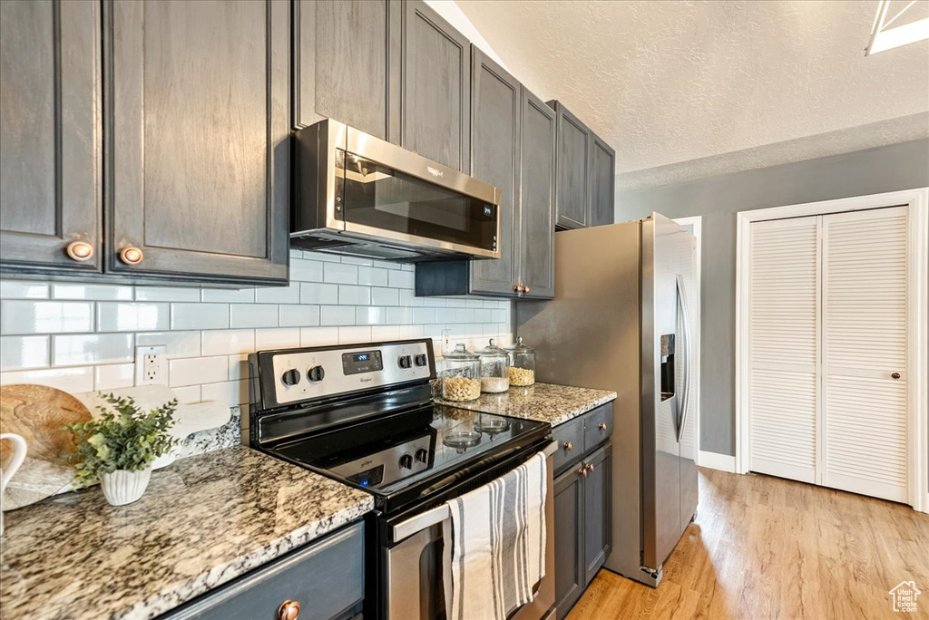 Kitchen featuring light stone countertops, backsplash, light hardwood / wood-style flooring, and stainless steel appliances