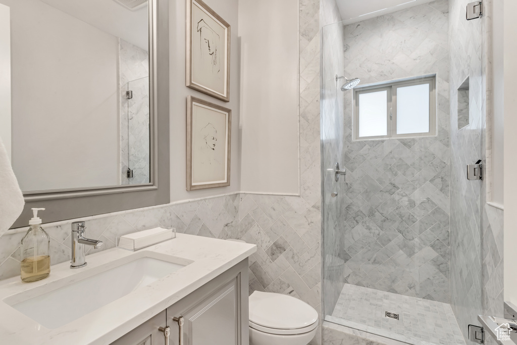 Bathroom featuring toilet, vanity, tasteful backsplash, tile walls, and a tile shower