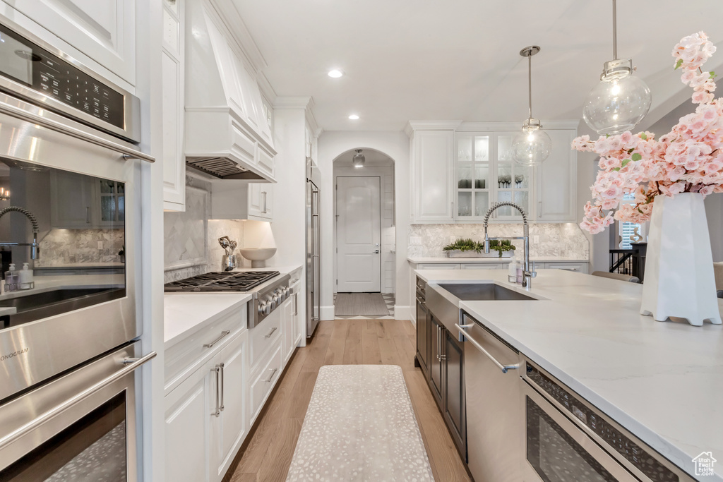 Kitchen with light hardwood / wood-style floors, decorative light fixtures, white cabinetry, backsplash, and custom range hood