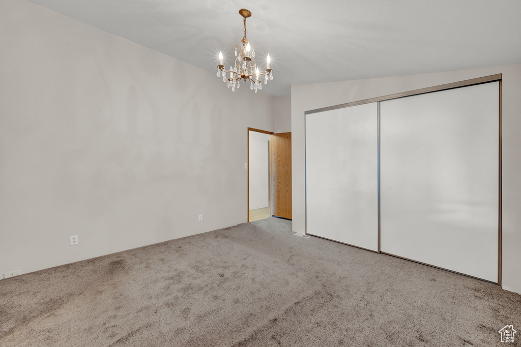 Unfurnished bedroom featuring light carpet, a closet, lofted ceiling, and an inviting chandelier