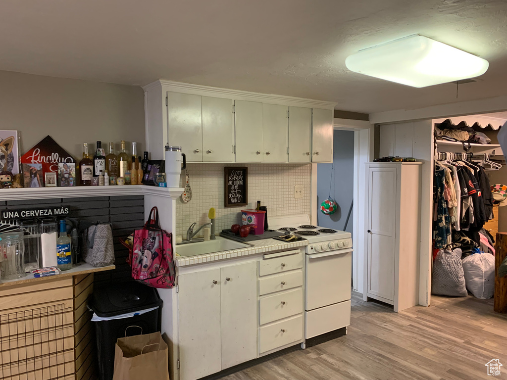 Kitchen featuring backsplash, white range oven, light wood-type flooring, and sink