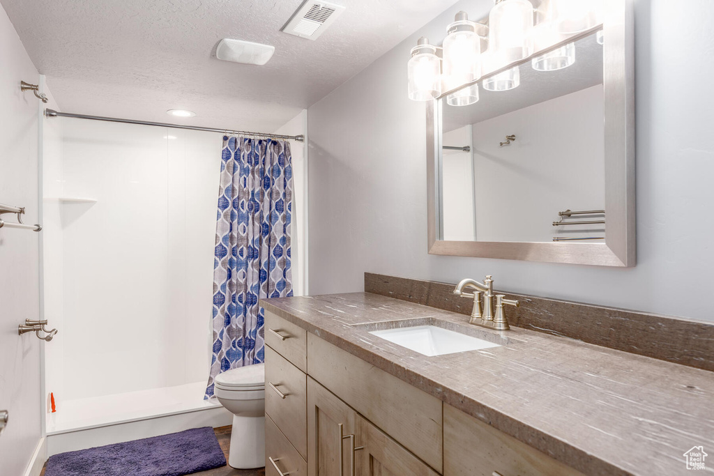 Bathroom with toilet, a textured ceiling, vanity with extensive cabinet space, and a shower with shower curtain