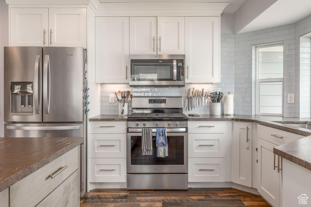 Kitchen with appliances with stainless steel finishes, white cabinetry, tasteful backsplash, and dark hardwood / wood-style flooring