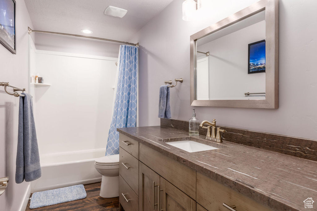 Full bathroom featuring hardwood / wood-style flooring, shower / bath combination with curtain, toilet, and oversized vanity