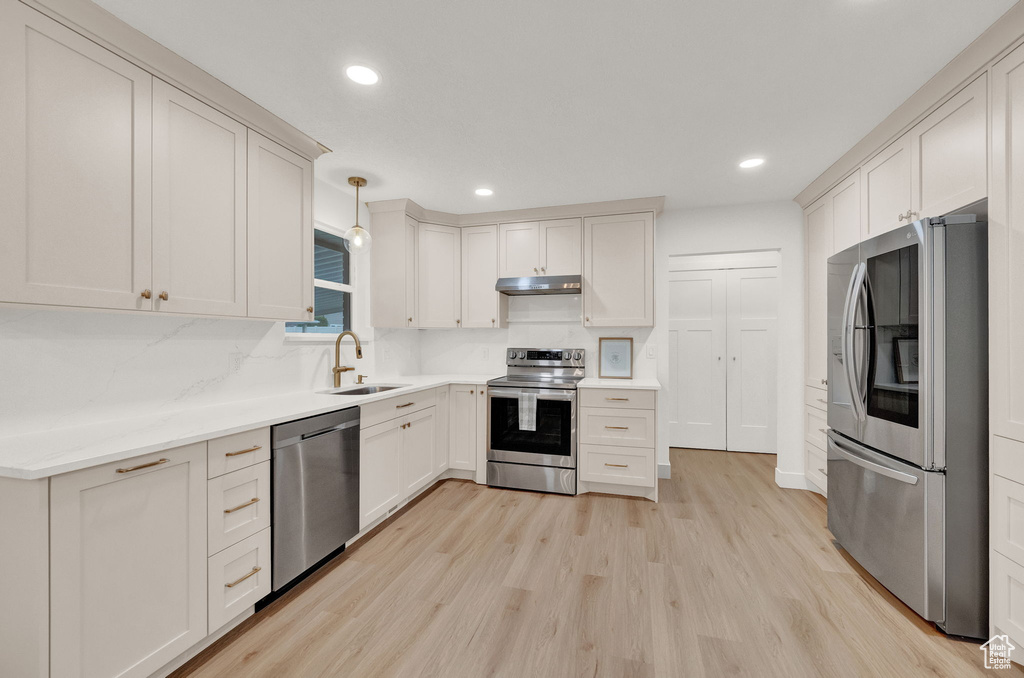 Kitchen with hanging light fixtures, light hardwood / wood-style flooring, stainless steel appliances, sink, and tasteful backsplash