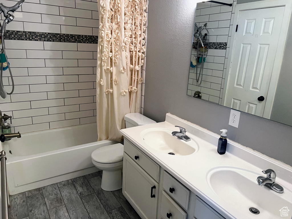 Full bathroom with double sink vanity, shower / bath combination with curtain, toilet, and hardwood / wood-style flooring