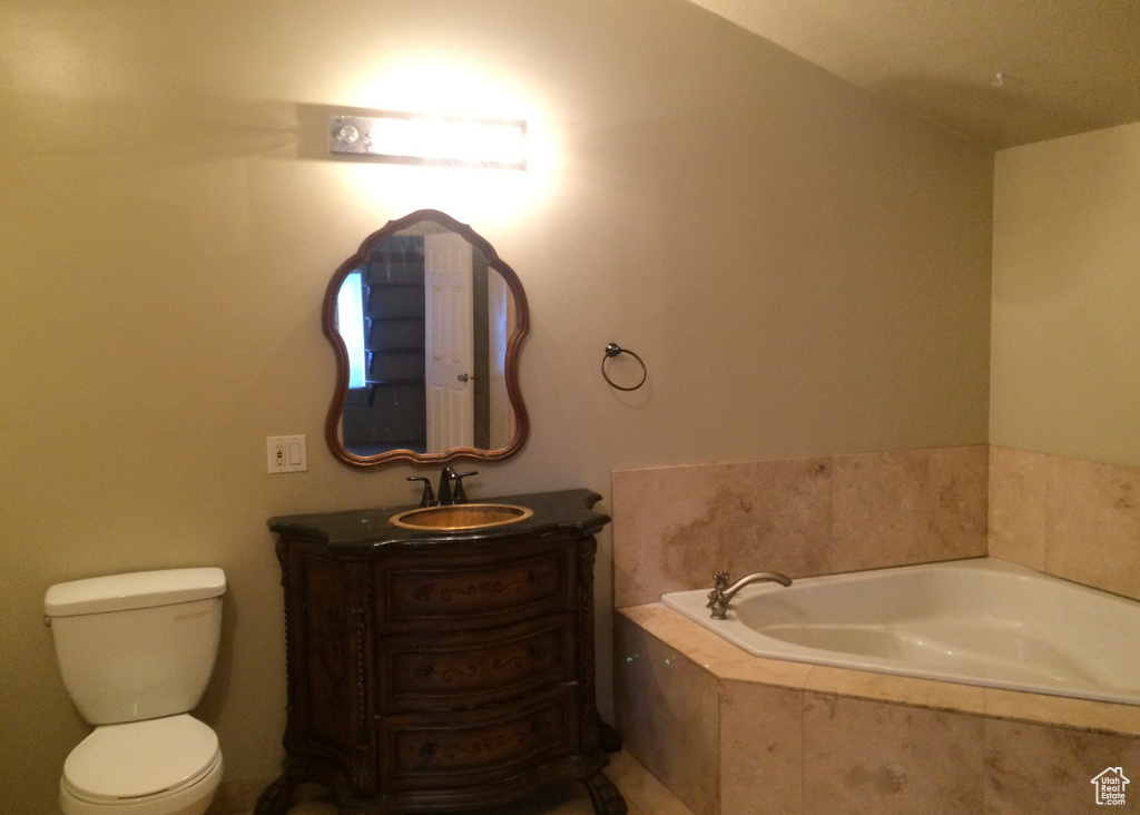 Bathroom with toilet, vanity with extensive cabinet space, lofted ceiling, and tiled tub