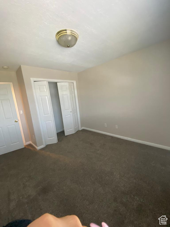 Unfurnished bedroom featuring a closet and dark carpet